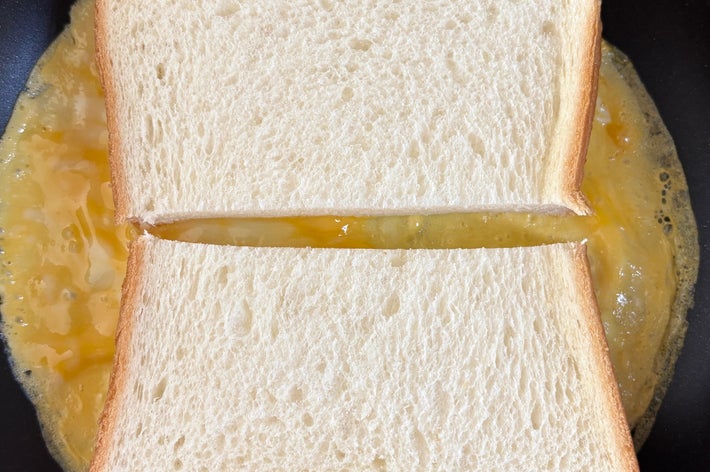 食パンの間に卵があり、フライパンで調理されているホットサンドの途中過程。