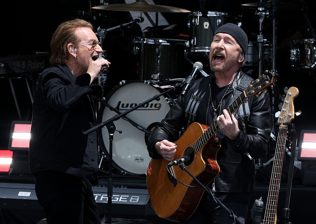 To musikere opptrer energisk på scenen, den ene synger og den andre spiller gitar. Trommer er synlige i bakgrunnen