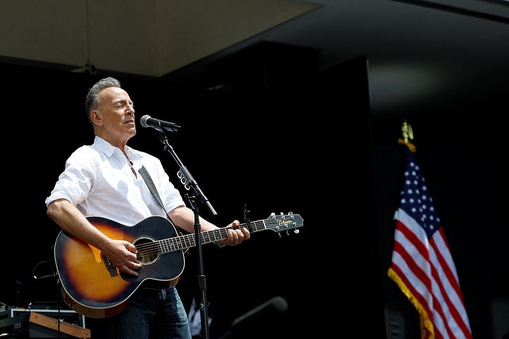 Musiker spiller gitar og synger på scenen med mikrofon, amerikansk flagg i bakgrunnen