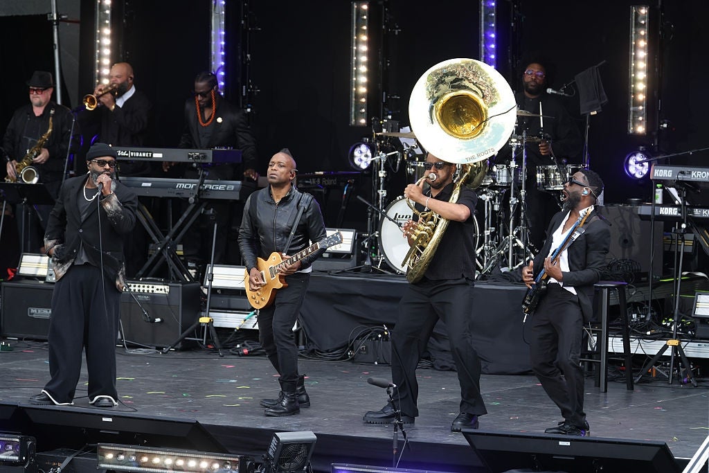 Musikere opptrer energisk på scenen med et brassband og elektriske gitarer, med en musiker som spiller en stor tuba