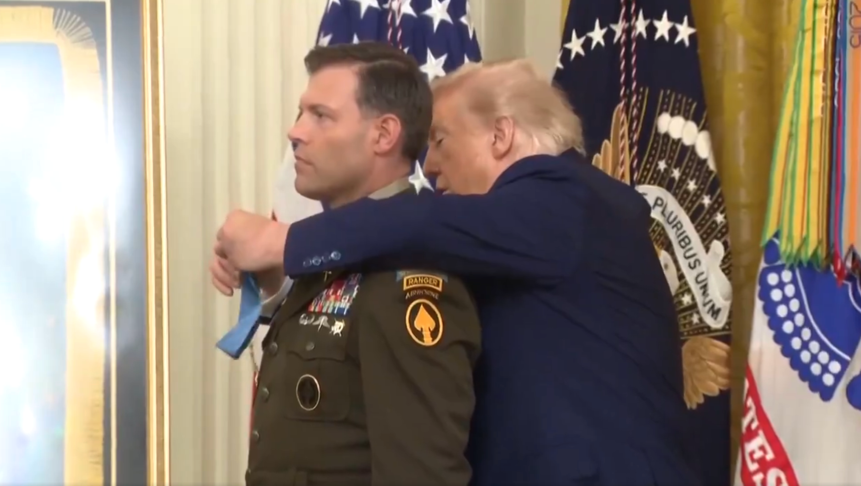 En person i militæruniform mottar en medalje fra en offentlig person i en formell seremonisetting