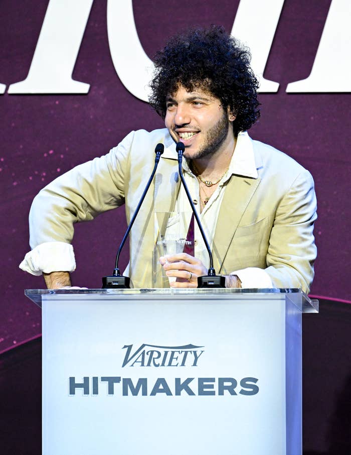 Benny Blanco in a suit with open collar shirt, smiling behind a podium with "Variety Hitmakers" sign