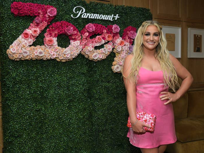 Person in a pink dress standing in front of a floral sign reading "Zoey" at a Paramount+ event