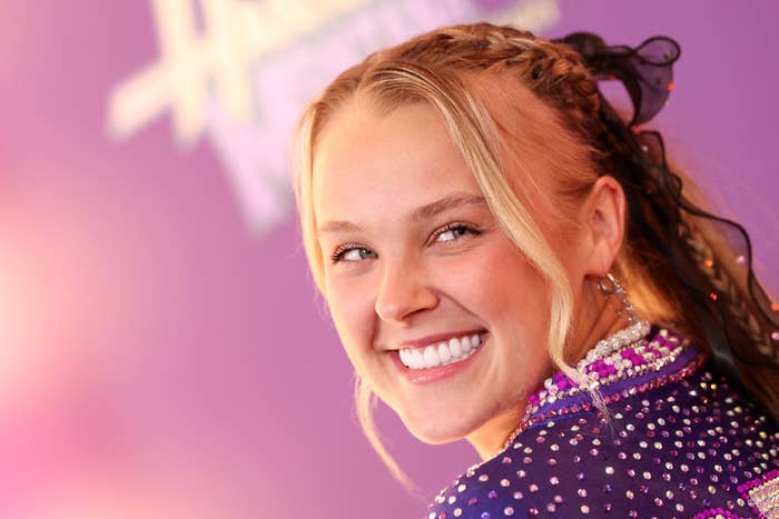 JoJo Siwa smiling at an event, wearing a beaded, sequined outfit with braided hairstyle