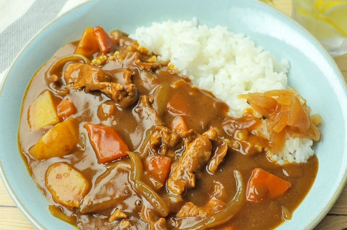 カレーライスの盛り付け。食欲をそそる野菜と肉が見え、爽やかな飲み物が横に置かれている。