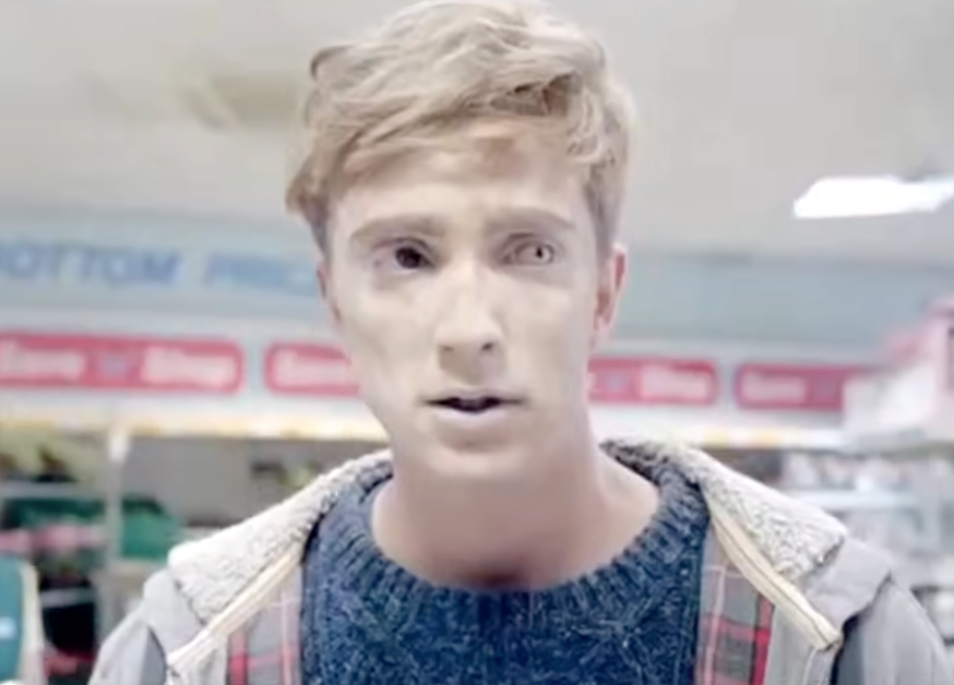 Person in a supermarket with powdered face and puzzled expression, wearing a sweater and jacket