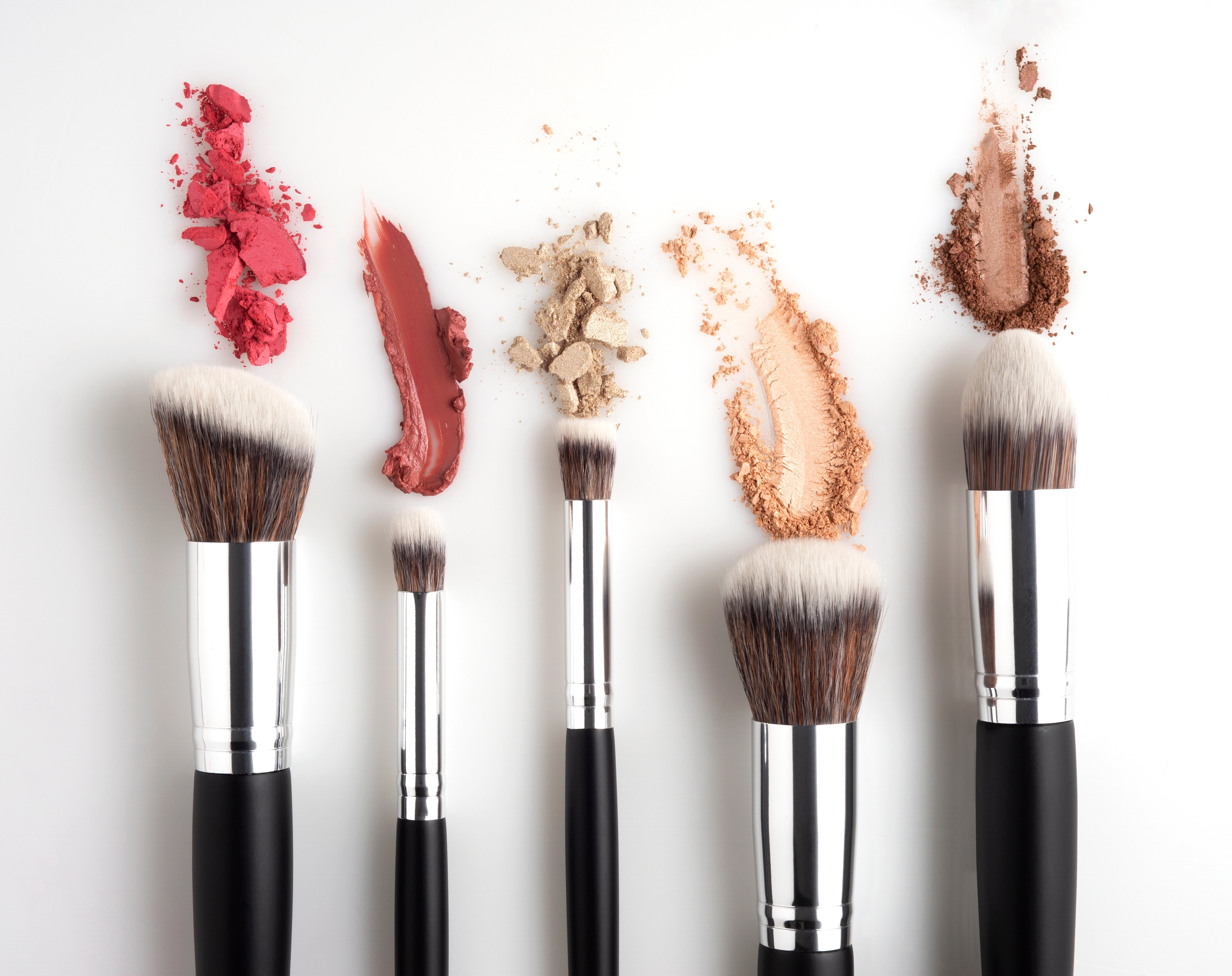 Makeup brushes with colorful crushed powders and creams connected a achromatic surface, showcasing quality tools and products