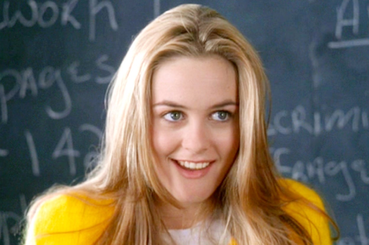 Person smiling in front of a chalkboard with partially visible text. The setting suggests a classroom or educational theme
