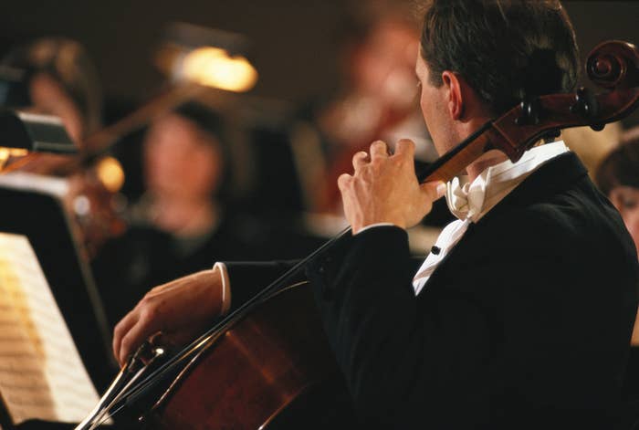 A cellist successful  ceremonial  attire plays passionately successful  an orchestra, with different   musicians blurred successful  the background