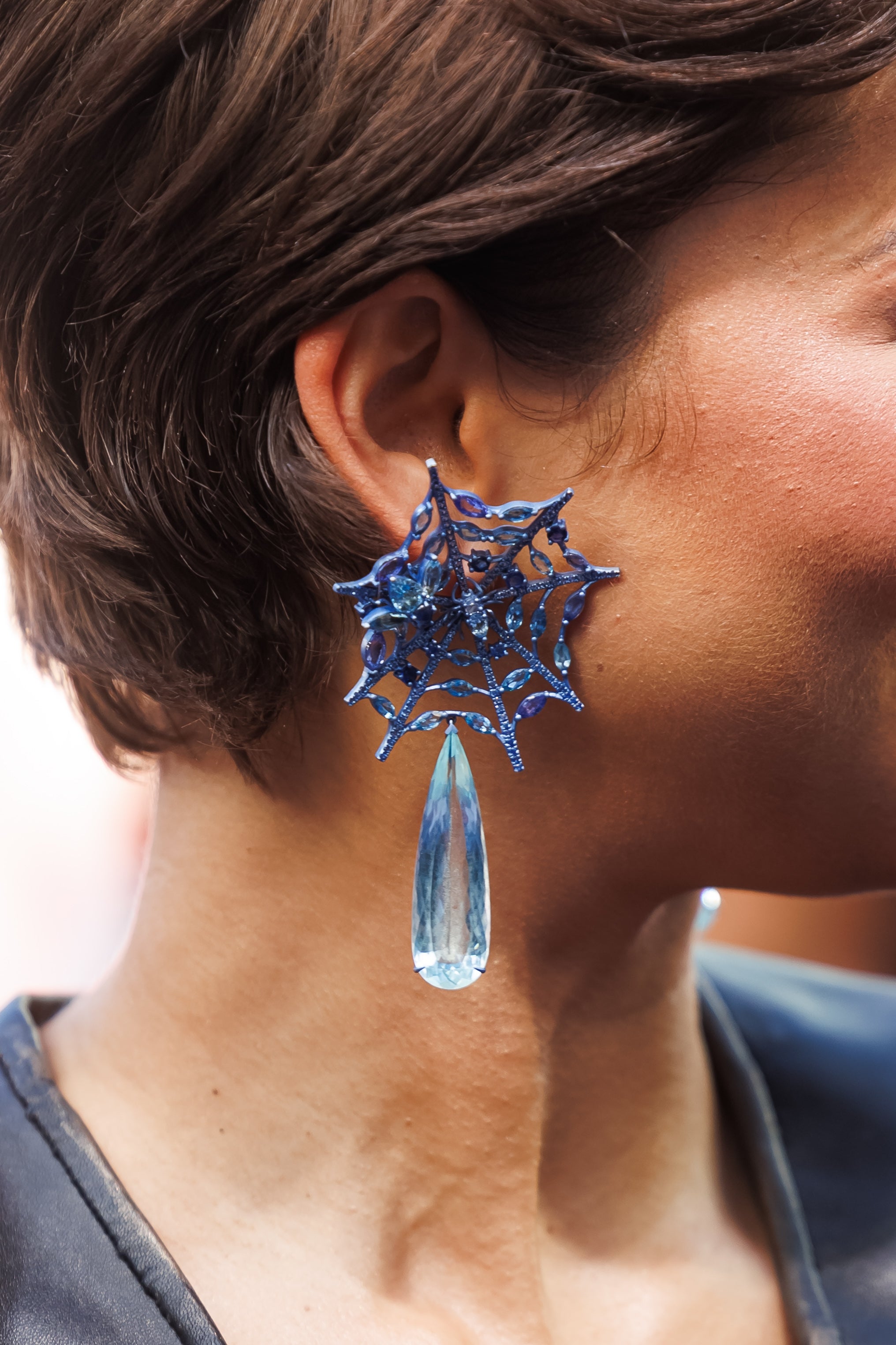 Zendaya wearing large spiderweb earrings with a teardrop gem, shown close-up against short hair