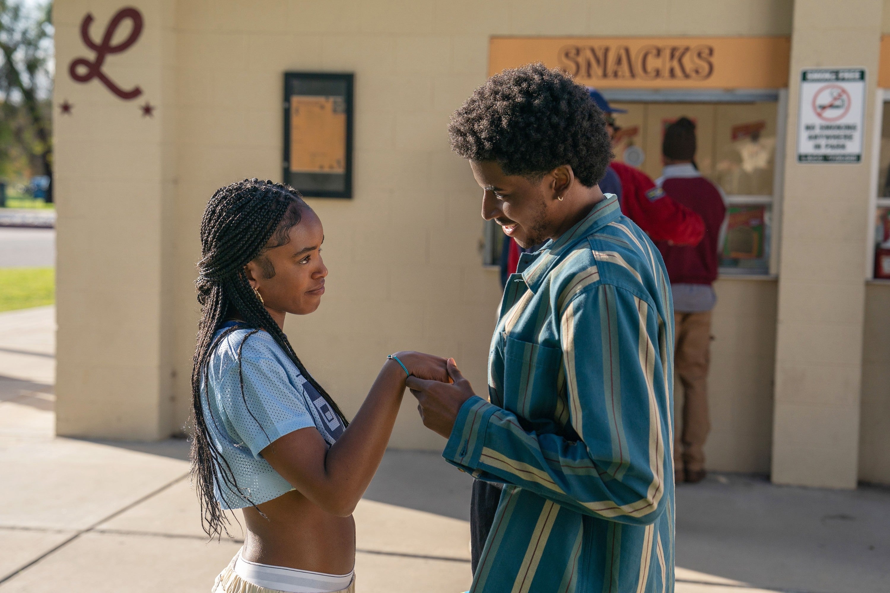 Two people stand outside a snack bar, holding hands. They are engaged in a warm conversation
