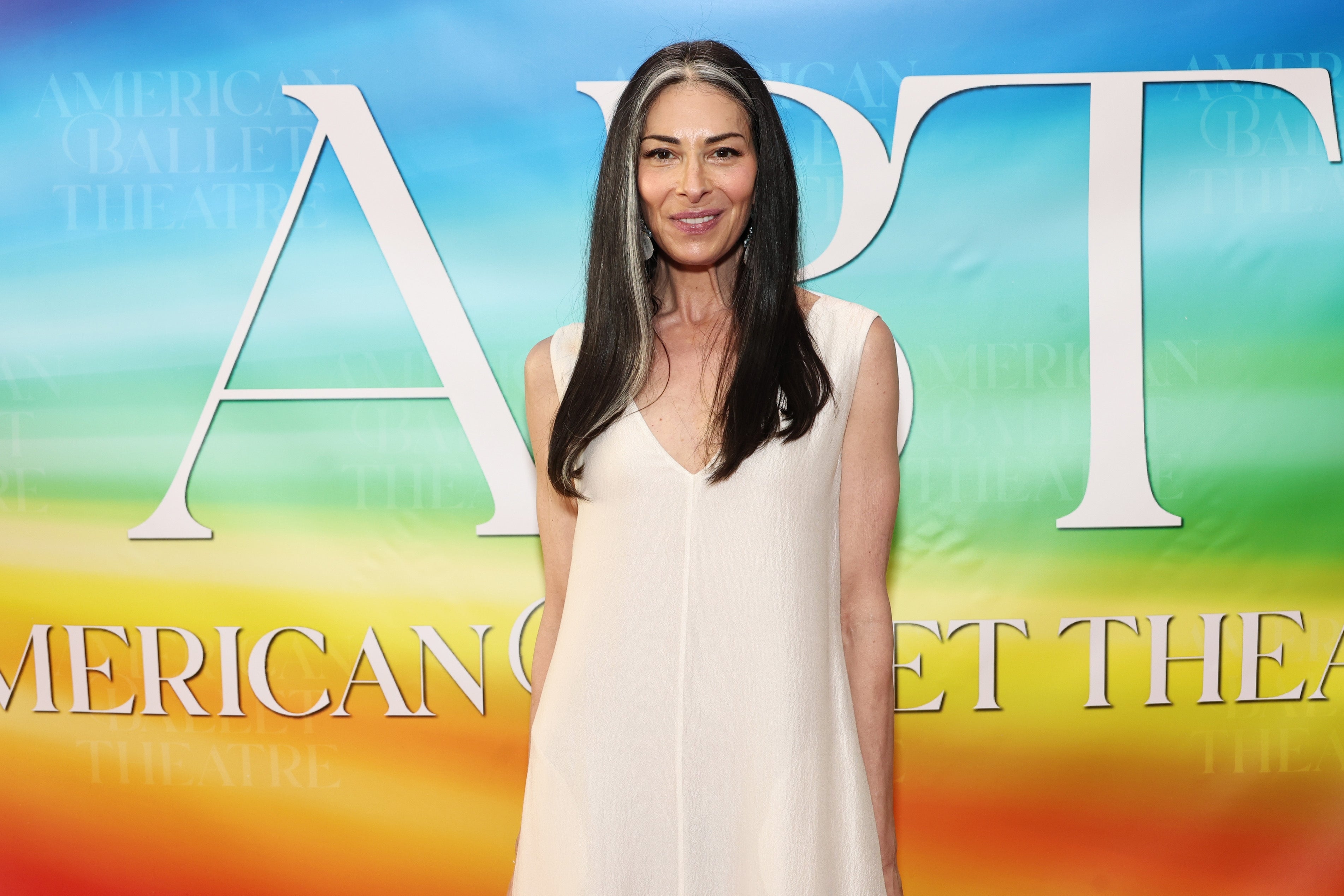Person successful a sleeveless, flowing formal poses astatine an lawsuit with a colorful backdrop displaying the substance "American Ballet Theatre."