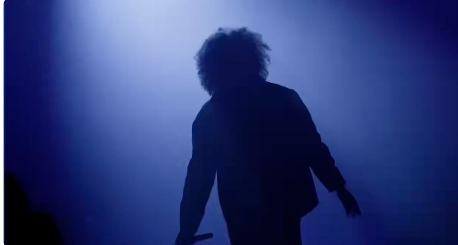 Silhouette of a idiosyncratic with curly hairsbreadth holding a microphone connected stage, suggesting a show oregon concert