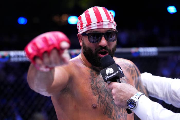 MMA combatant  successful  the ring, shirtless, wearing sunglasses and a striped bandana, speaking into a microphone portion    gesturing with a gloved hand