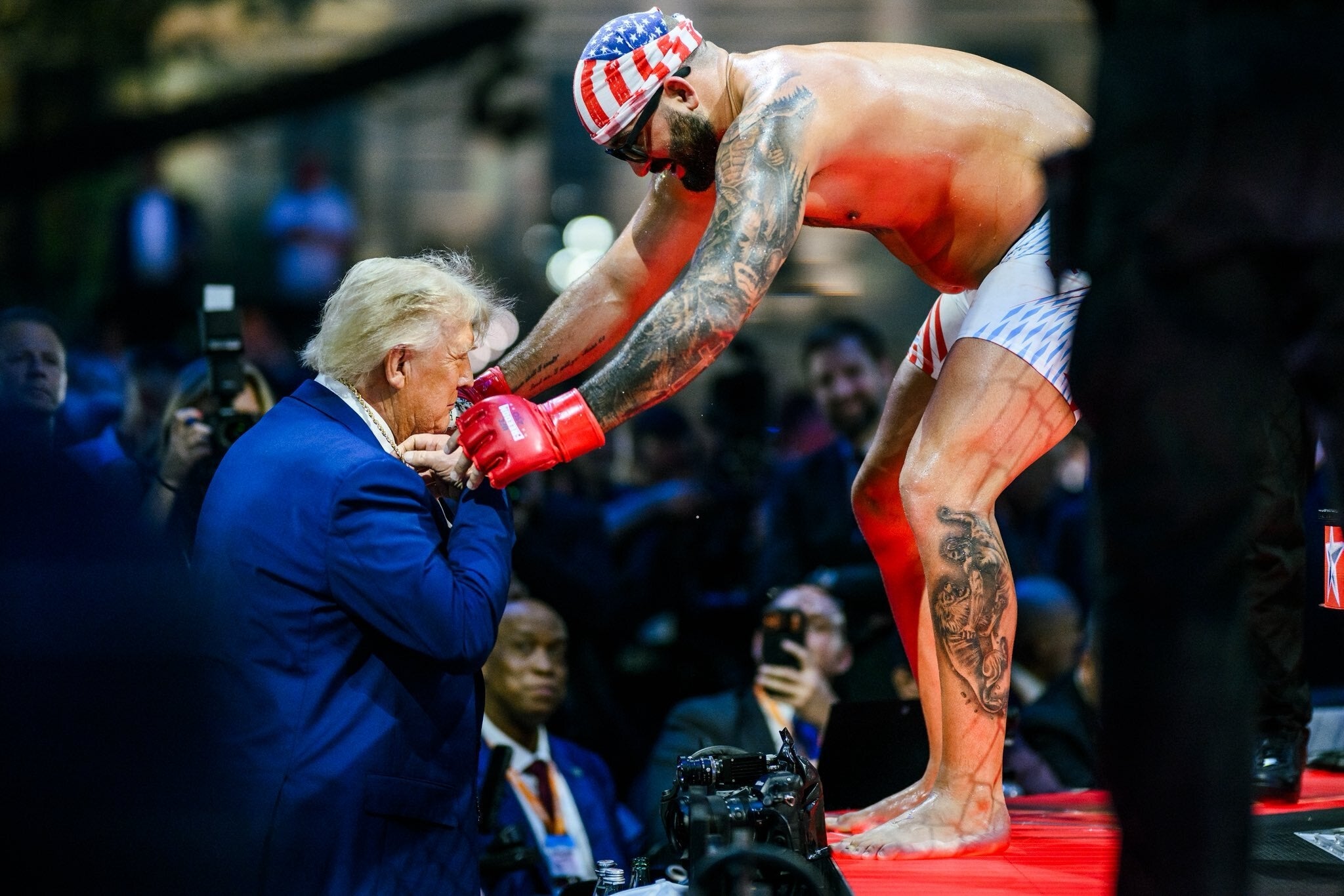 Man successful boxing cogwheel leans down to talk with a antheral successful a suit successful a crowded lawsuit setting