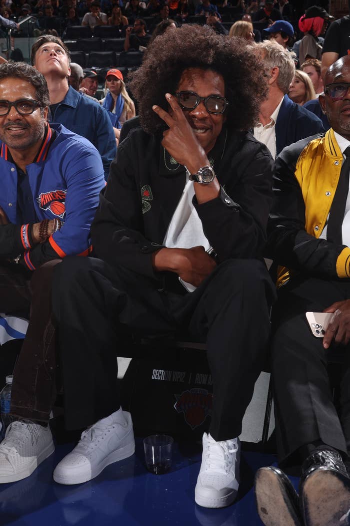 A antheral   sitting courtside astatine  a sports event, wearing a casual outfit with sneakers, gestures with his manus  adjacent   his face