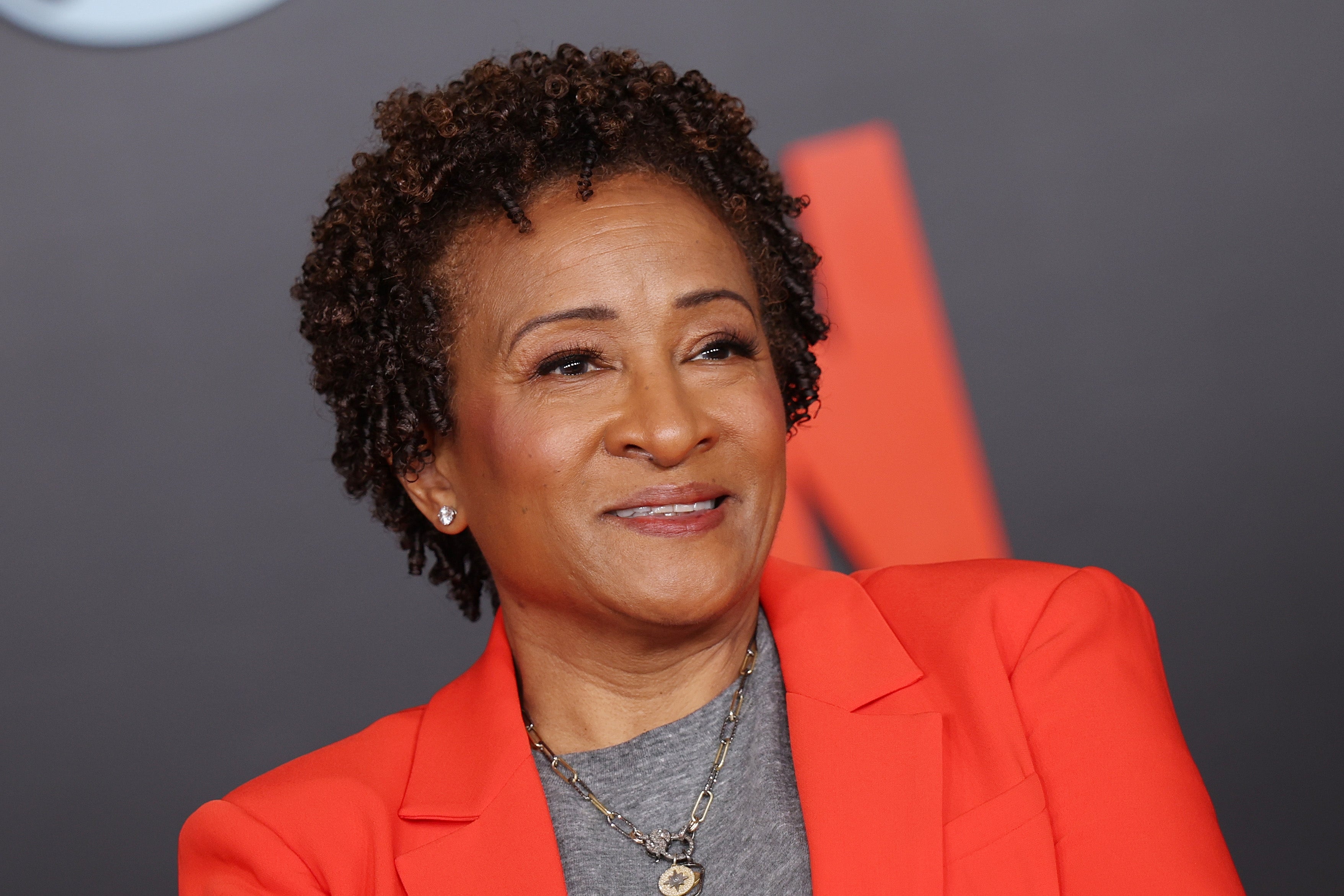 A idiosyncratic smiling, wearing a stylish blazer implicit a casual shirt, connected a media lawsuit backdrop