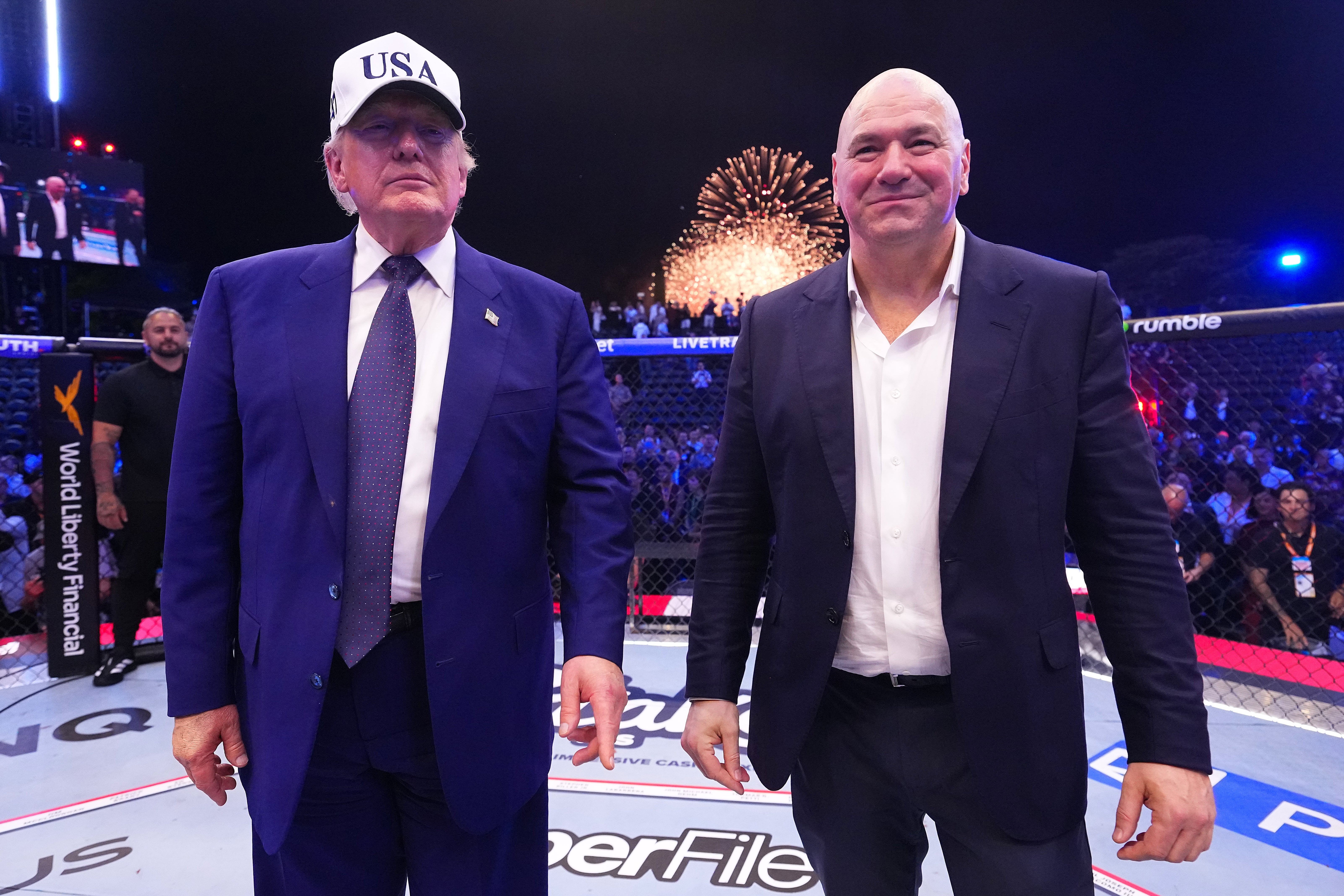 Two men lasting successful an MMA ring, 1 wearing a shot headdress and suit, the different successful a suit without a tie. Fireworks successful the background