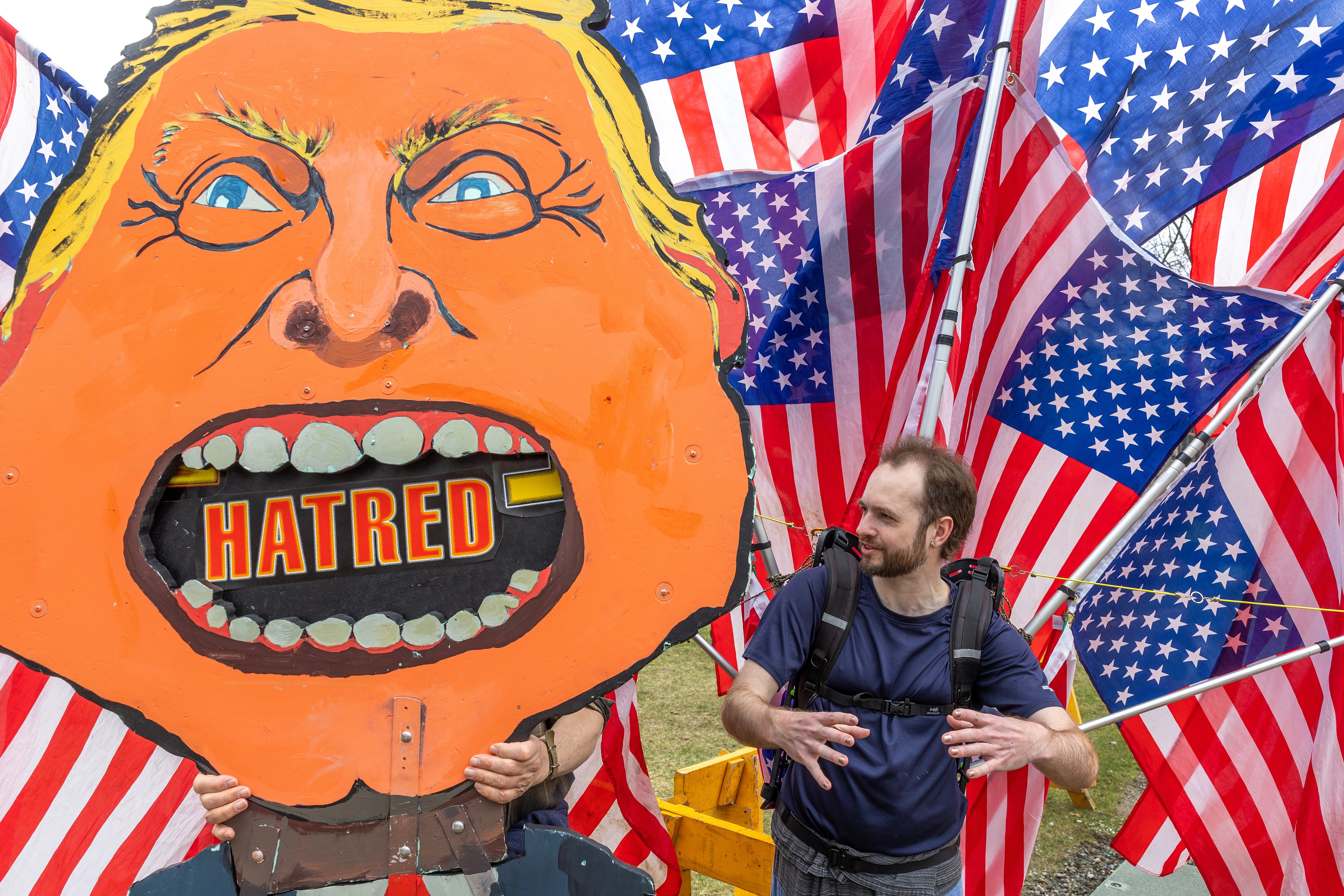 Man holding a caricature of a person   with "hatred" successful  the mouth, surrounded by American flags