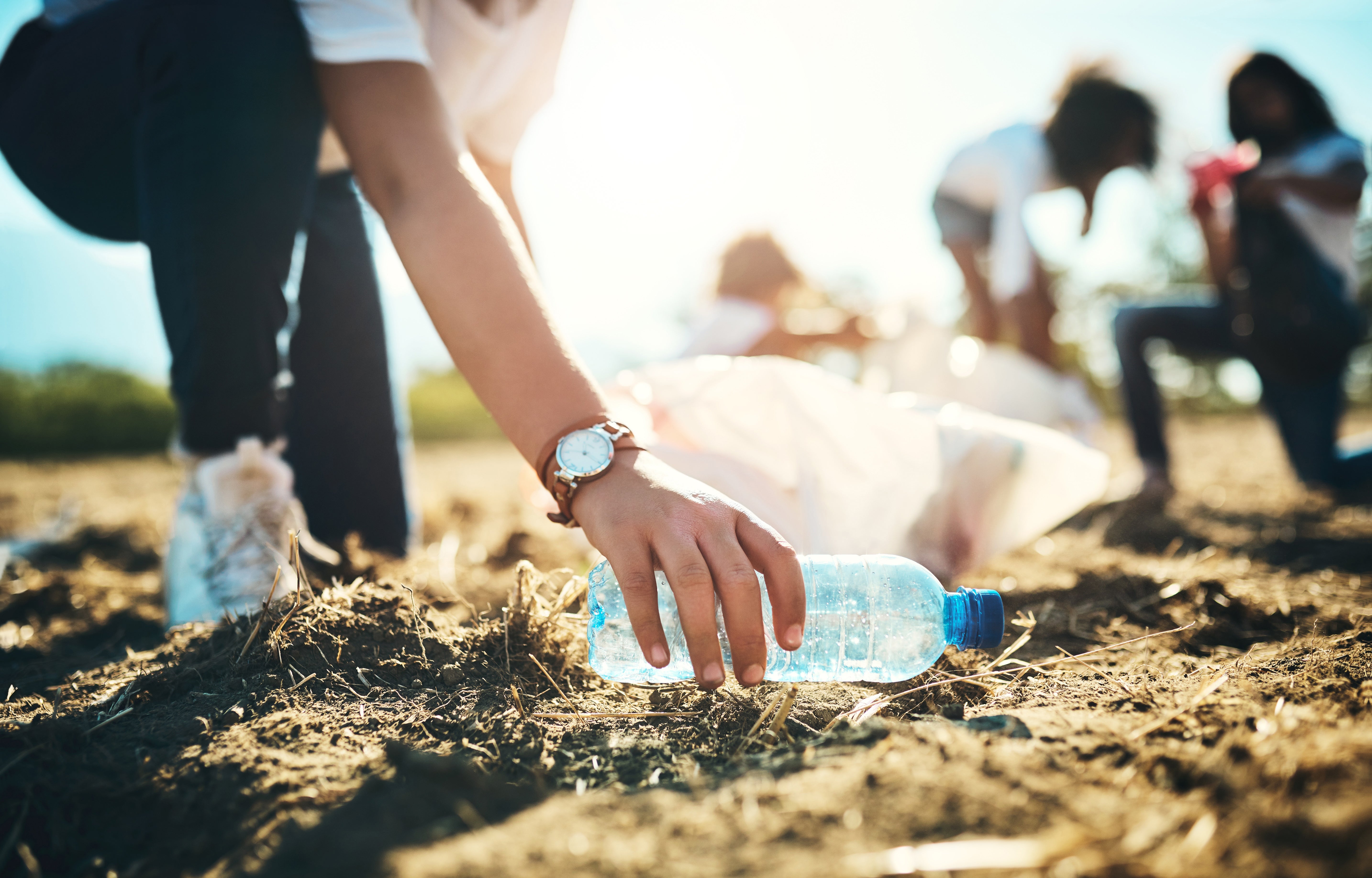 Person picking up   a integrative  vessel  during a assemblage  cleanup event, with others collecting trash successful  the background