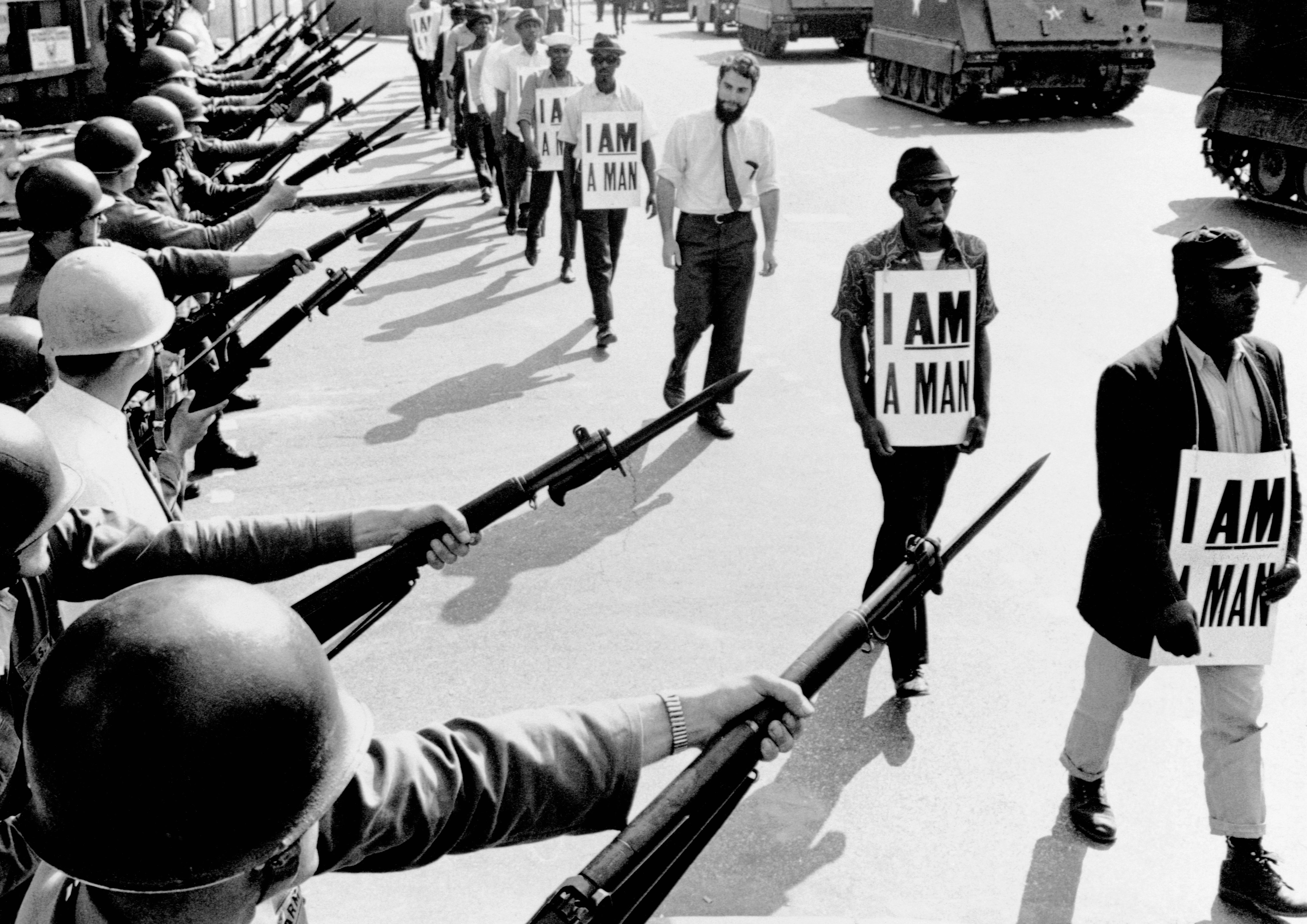 Civil rights protesters holding "I Am a Man" signs look   National Guard soldiers with rifles during a march