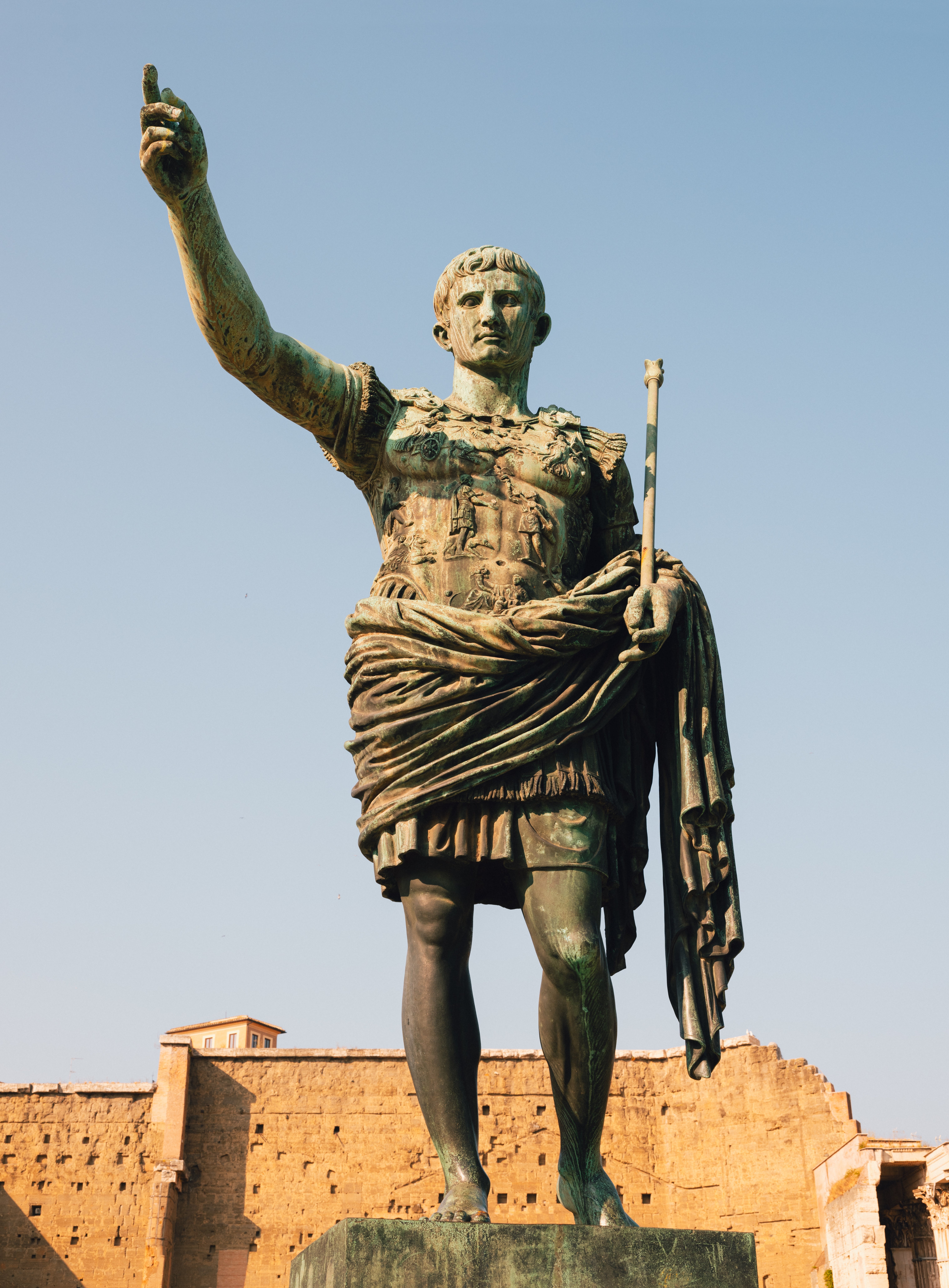 Ancient Roman statue of an emperor, perchance  Augustus, with a raised arm. The fig  is successful  accepted   Roman attire, with elaborate  armor and a draped cloak