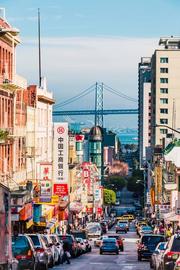Bustling thoroughfare  successful  San Francisco's Chinatown with signs, shops, and distant   presumption    of the Bay Bridge