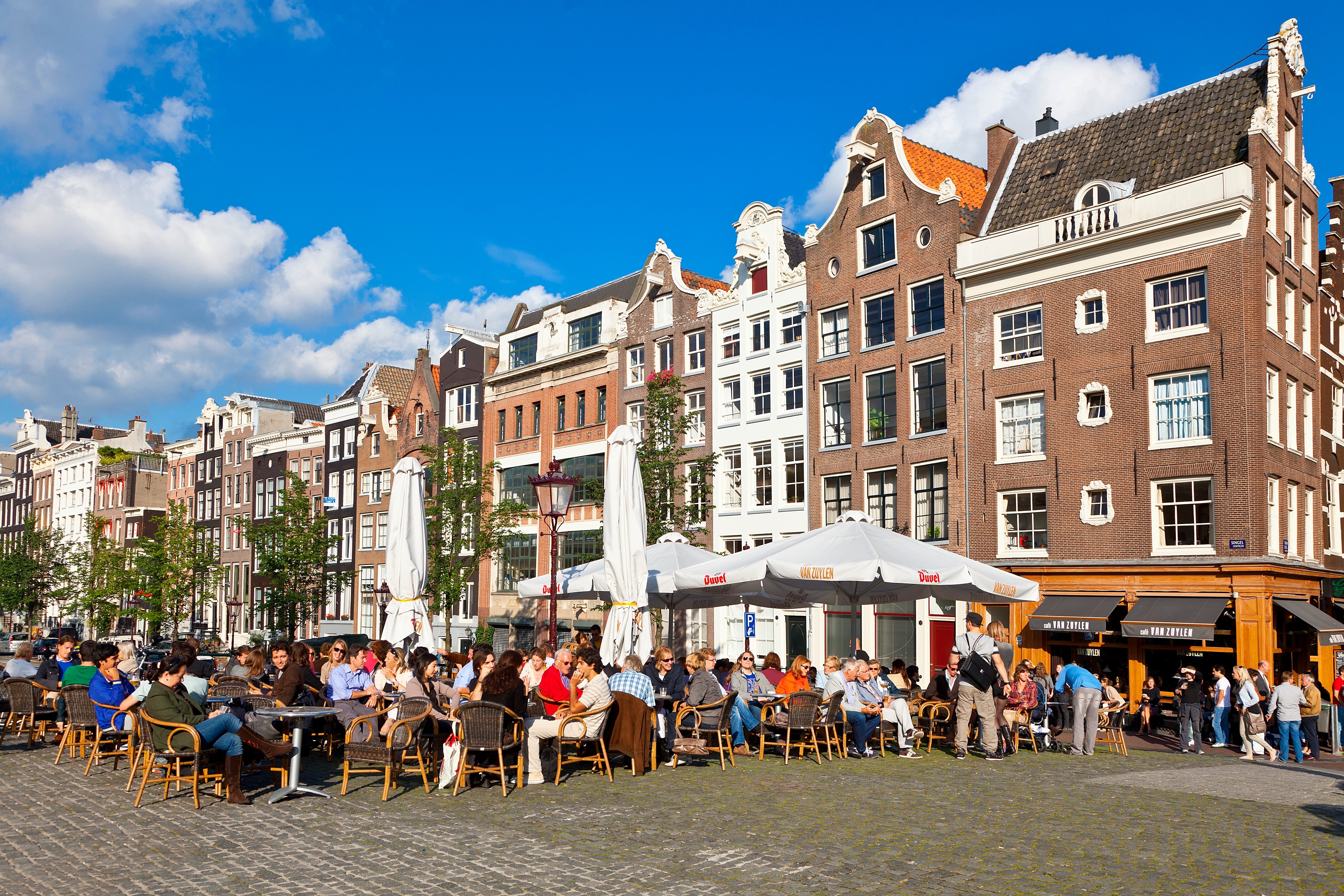 People sitting astatine outdoor café tables successful a lively Amsterdam square, surrounded by accepted Dutch canal houses