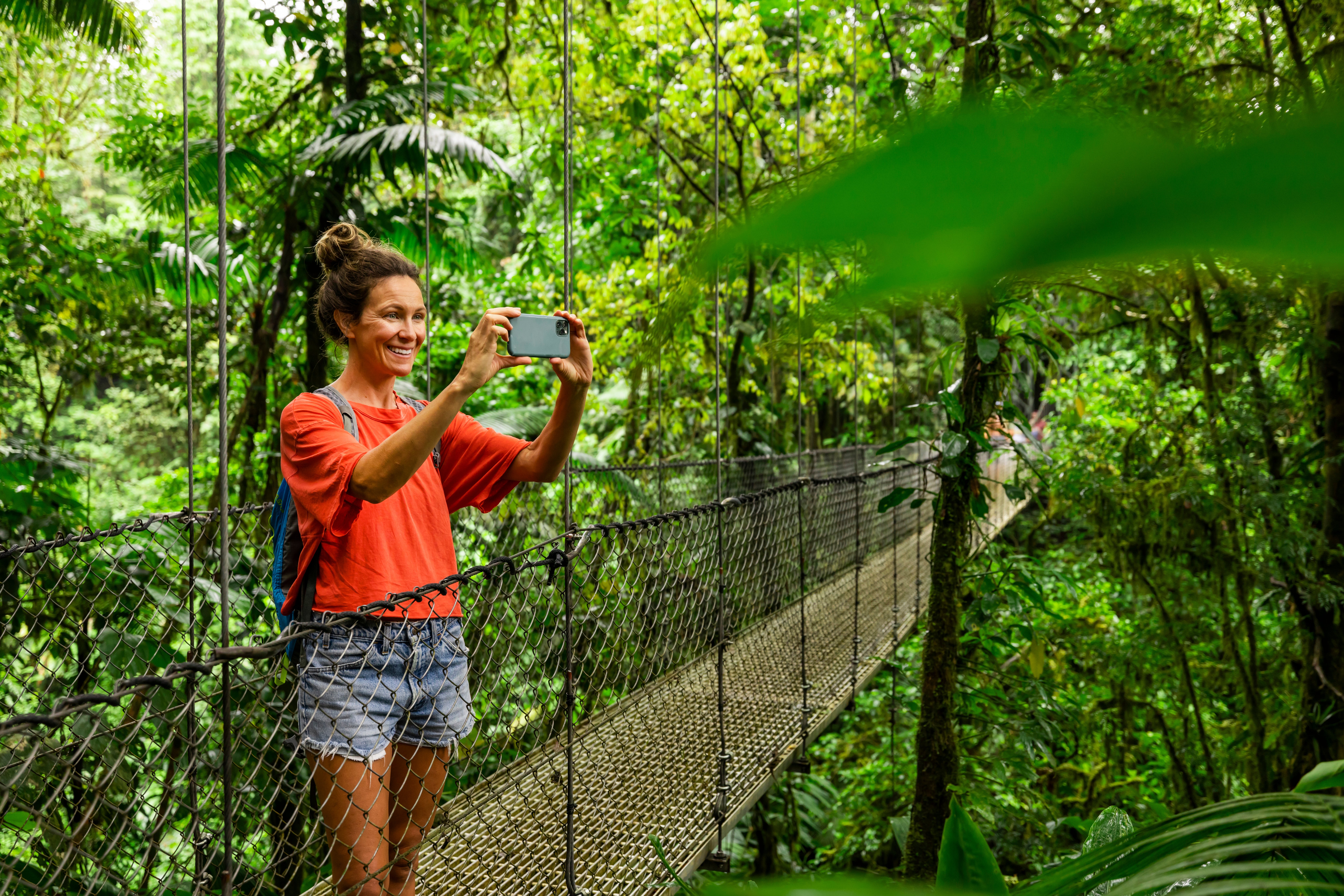A idiosyncratic takes a photograph portion lasting connected a suspension span successful a lush, tropical forest, capturing the scenic view