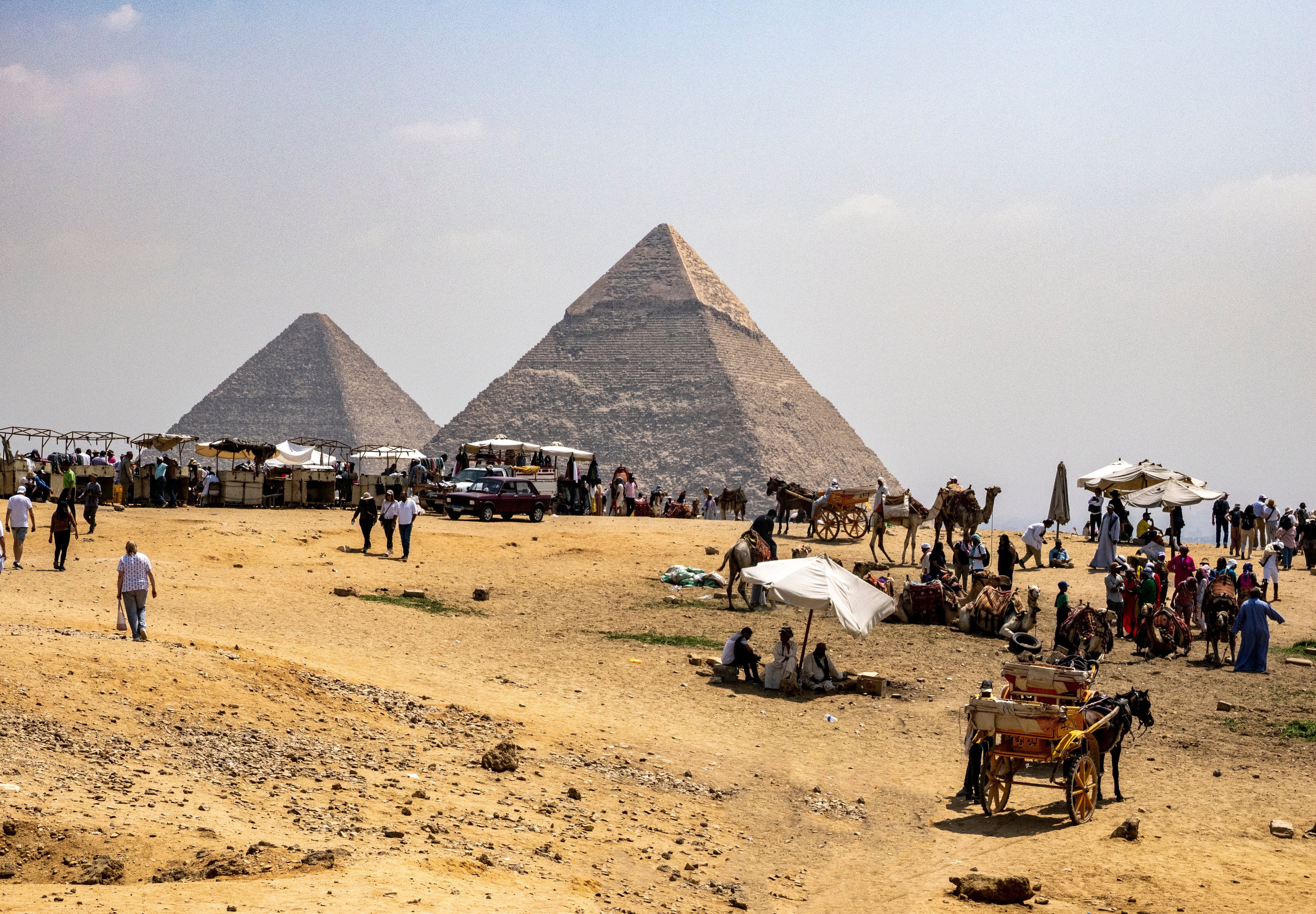 Tourists and vendors stitchery successful beforehand of the Pyramids of Giza nether a wide sky, highlighting question and taste exploration