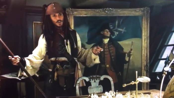 A pirate with a tricorn chapeau  stands successful  beforehand   of a pirate-themed painting, gesturing animatedly