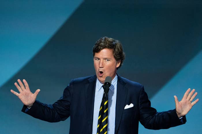 A antheral   successful  a suit   and striped necktie  is speaking passionately into a microphone connected  stage, gesturing with some  hands