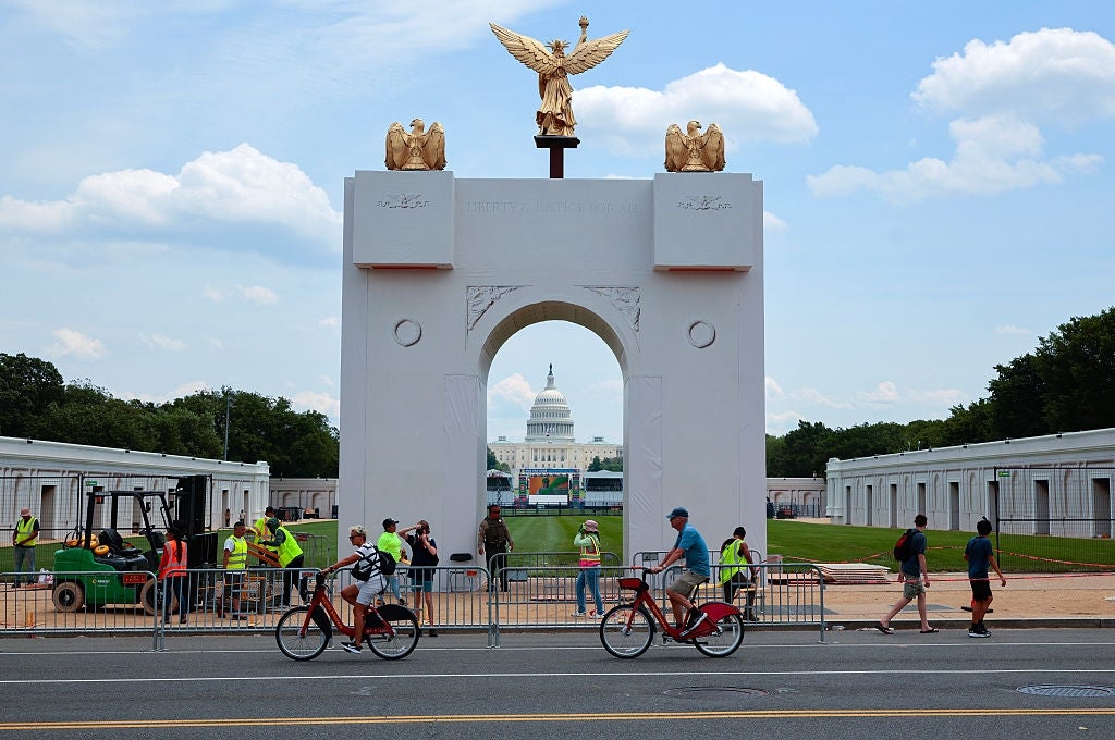 Folk går og sykler forbi en midlertidig bue med gyldne statuer, med US Capitol synlig gjennom buen i bakgrunnen
