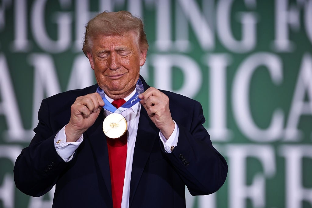 Mann i dress holder opp en stor medalje. Bakgrunnsteksten lyder