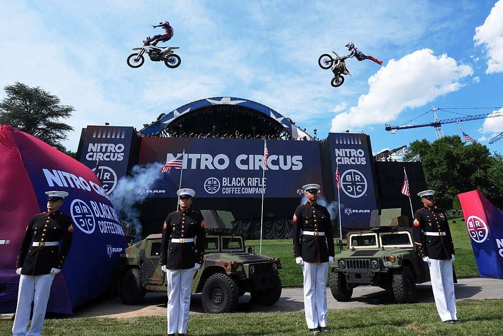 Motorsyklister utfører luftstunt over militært personell og kjøretøy på et Nitro Circus-arrangement