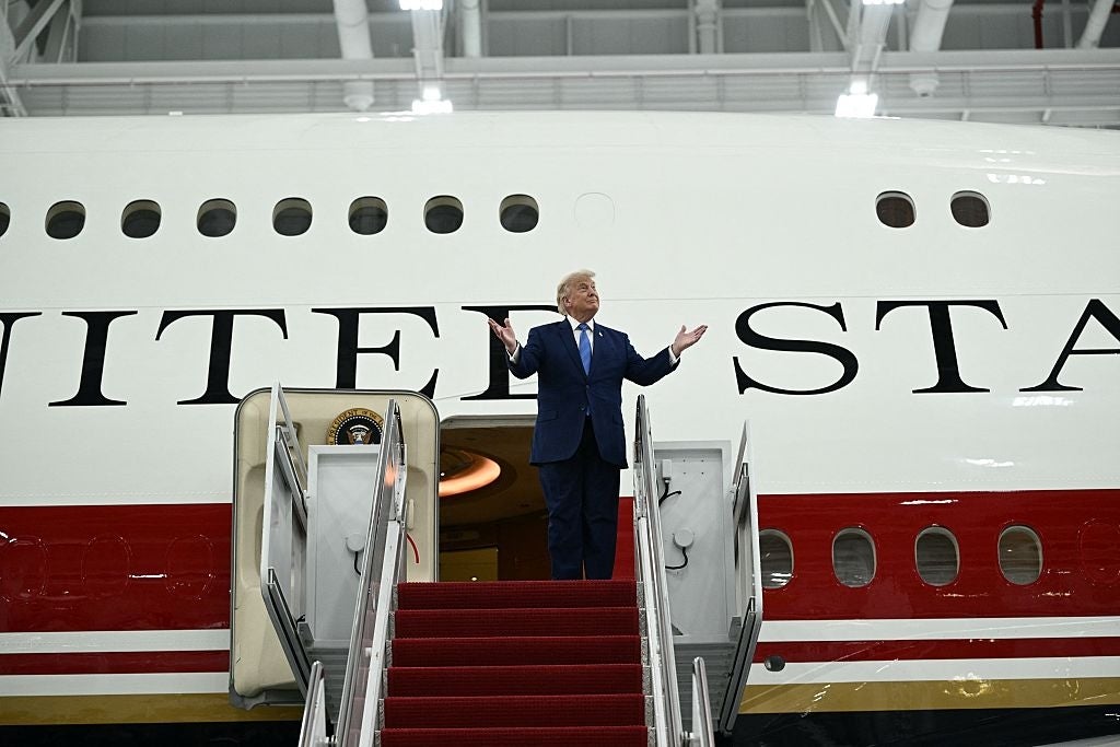 En person i dress står på trappene til et stort fly, med armene åpne