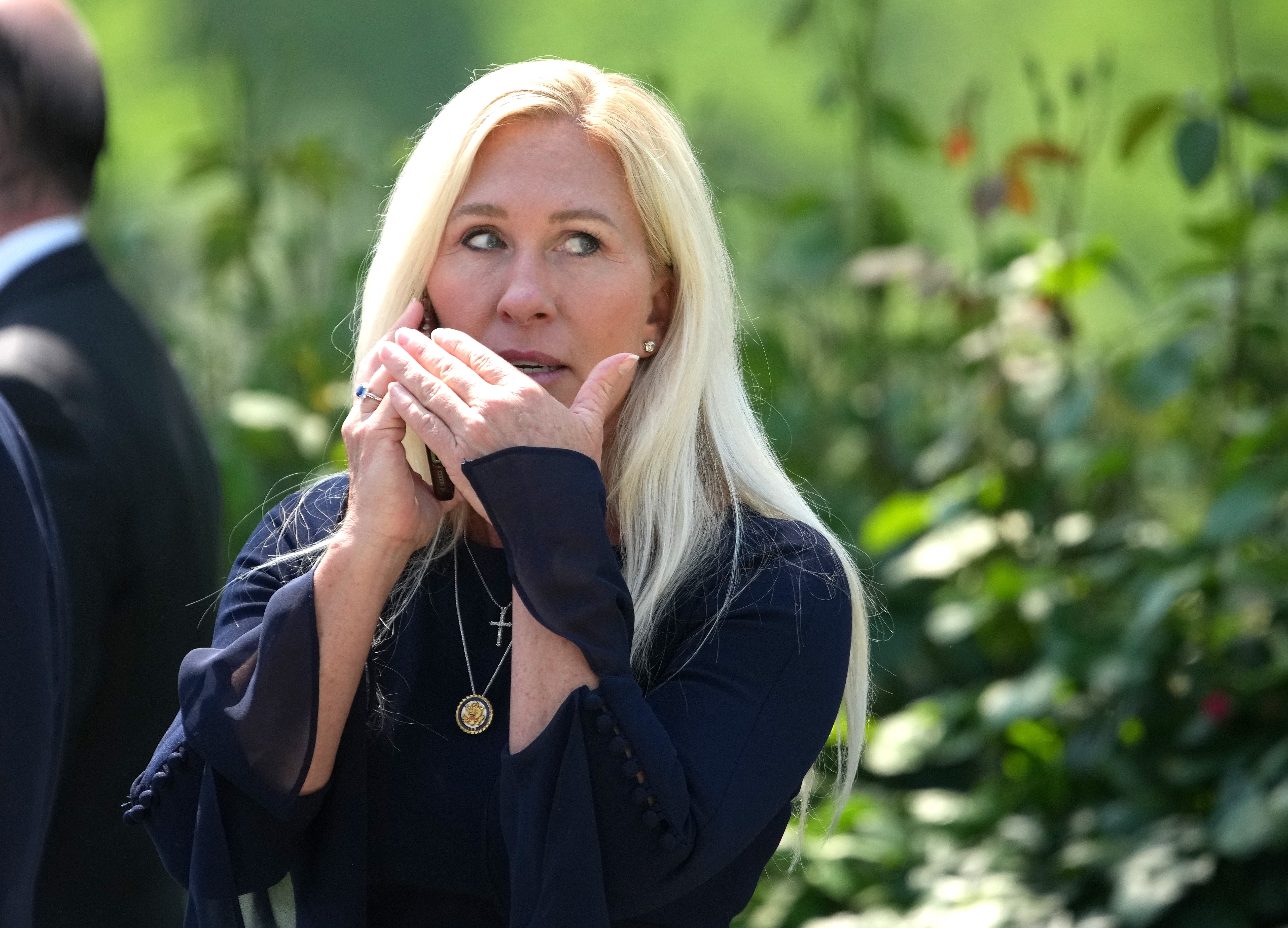 Person with agelong hairsbreadth utilizing a telephone outdoors, looking to the side, wearing a acheronian long-sleeve apical and a pendant necklace