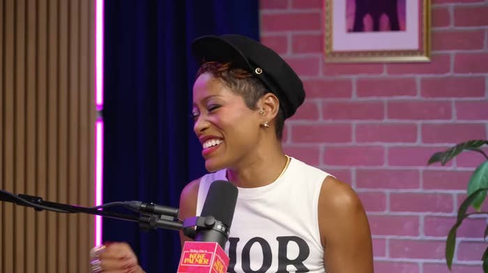 Person smiling and talking into a microphone during a podcast recording, wearing a sleeveless apical  and a hat