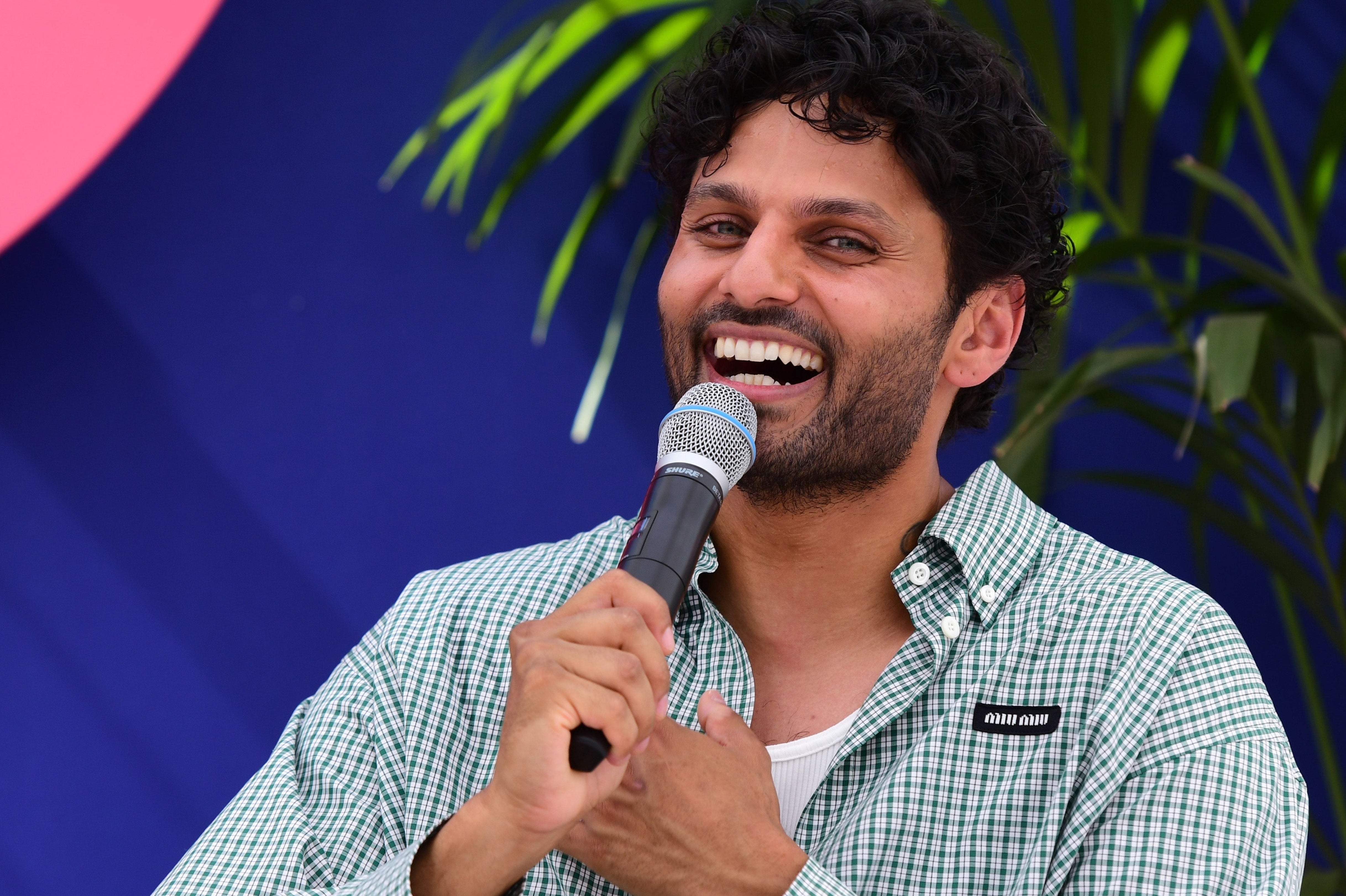 A idiosyncratic connected signifier holds a microphone, smiling portion dressed successful a casual checkered shirt