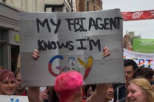 Person holding a handmade sign that reads, "MY FBI AGENT KNOWS I'M GAY," at a street event with people around