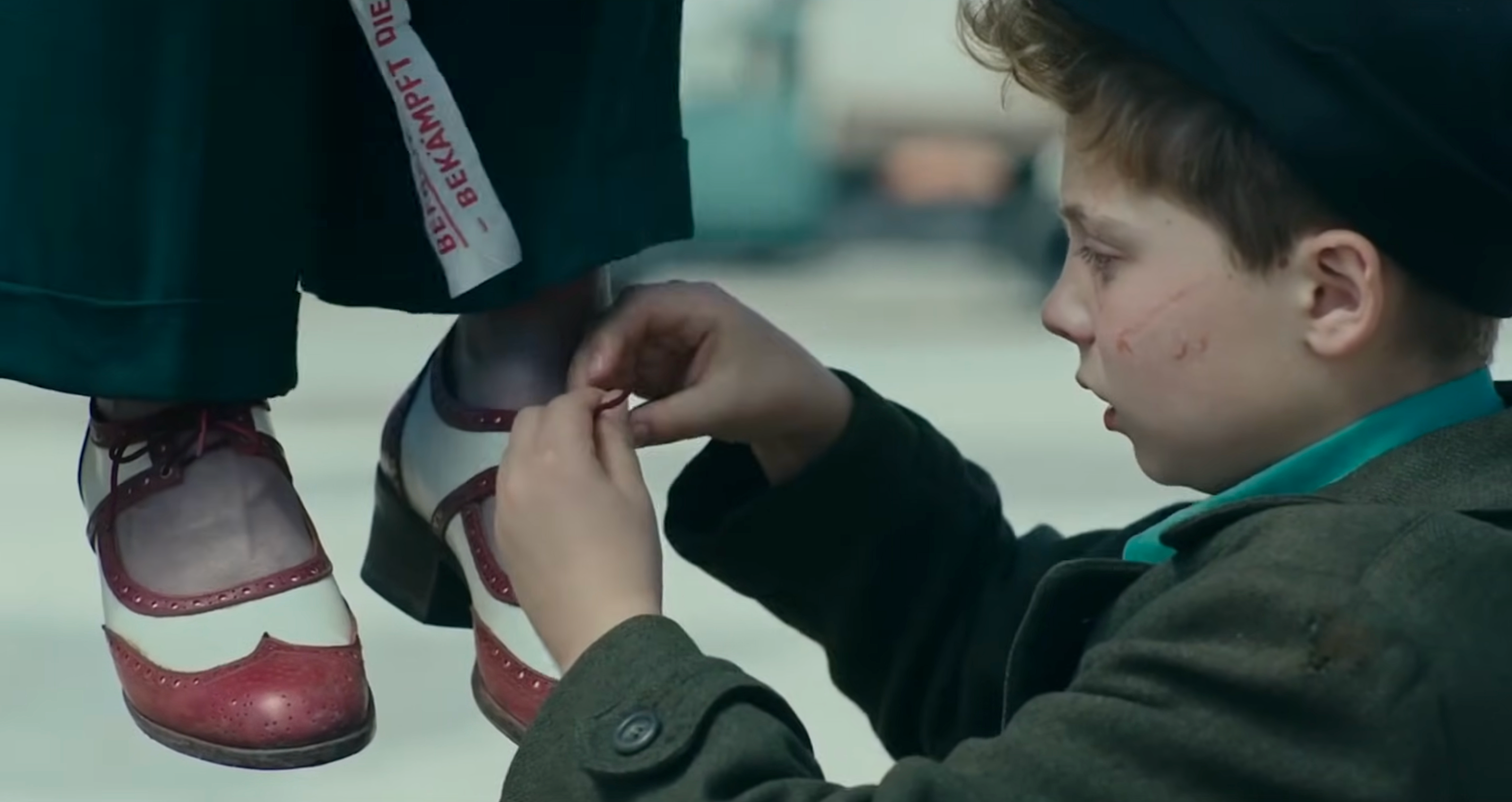 A kid  ties the shoelaces of his parent  who was publically  hanged successful  Nazi Germany