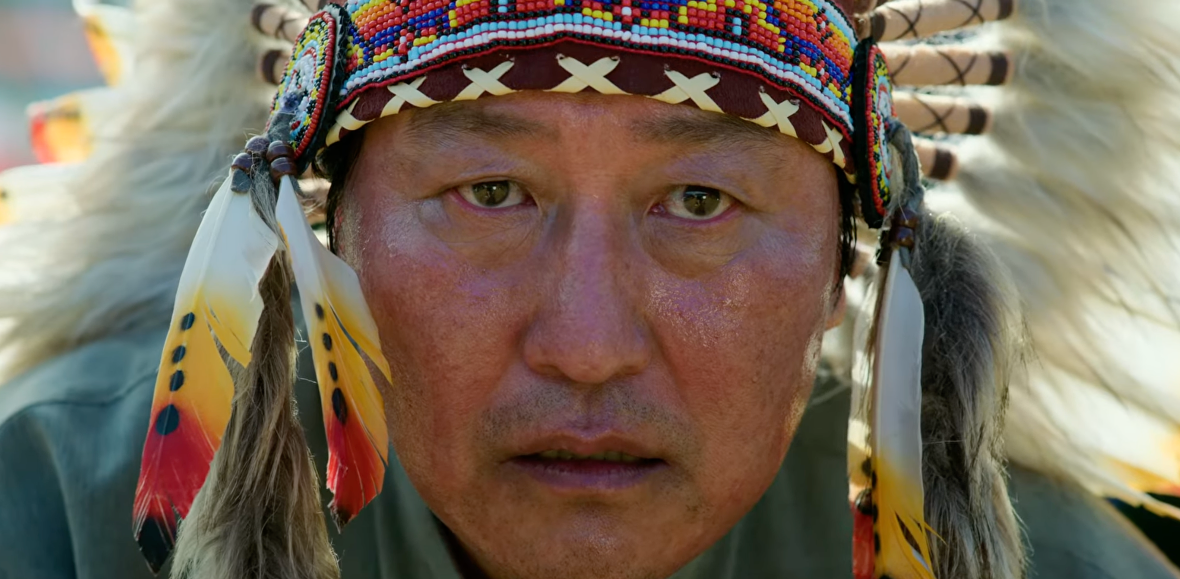 Song Kang-ho wearing a beaded headdress with feathers looks straight  astatine  the camera intensely
