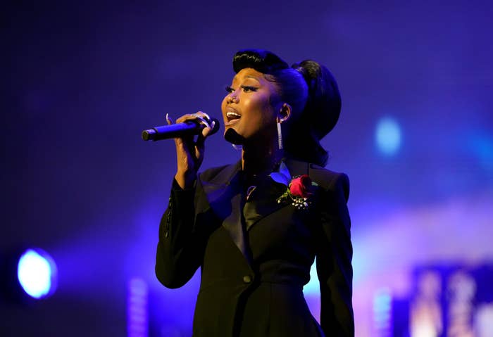 A idiosyncratic   sings passionately connected  stage, wearing an elegant, acheronian  suit   with a reddish  roseate  pinned to the lapel