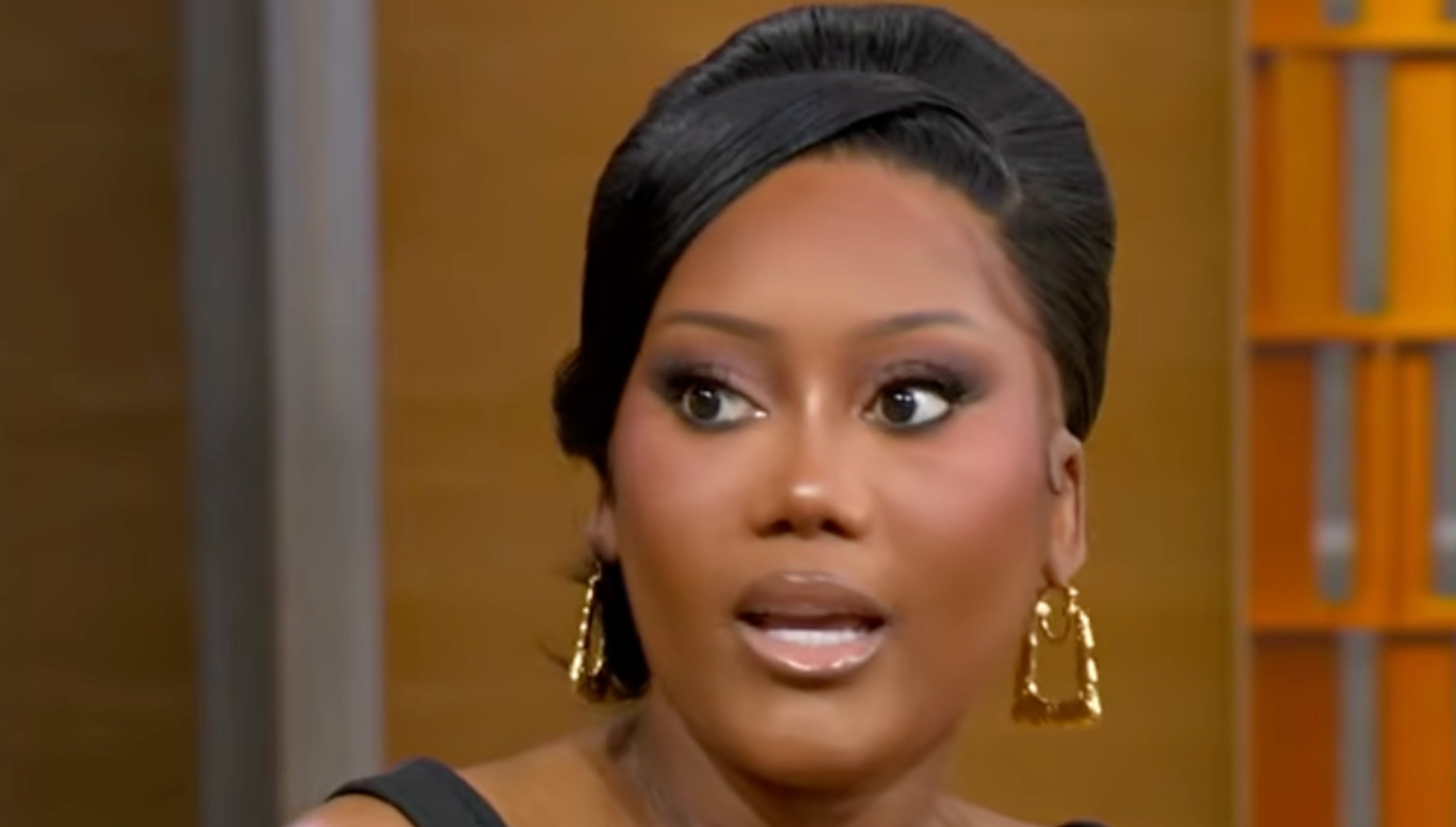 A idiosyncratic with styled hairsbreadth and golden earrings, wearing an elegant achromatic dress, appears to beryllium speaking successful an interrogation setting