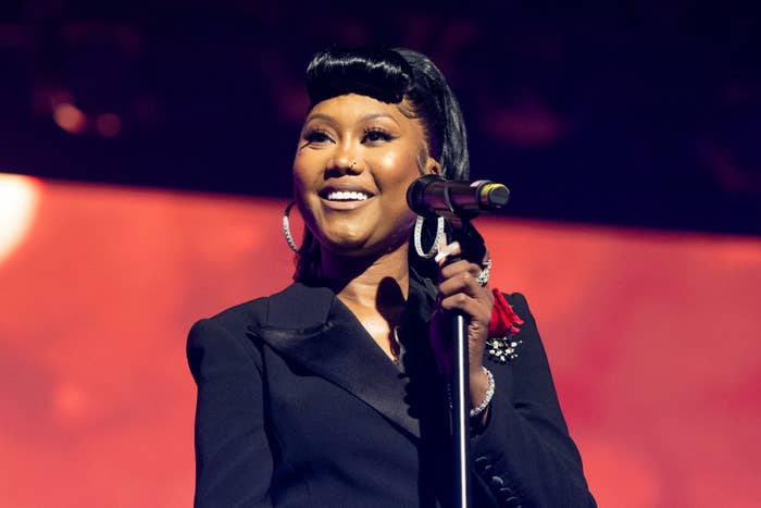 Celebrity smiling connected  stage, wearing a tailored achromatic  suit   and hoop earrings, holding a microphone during a performance