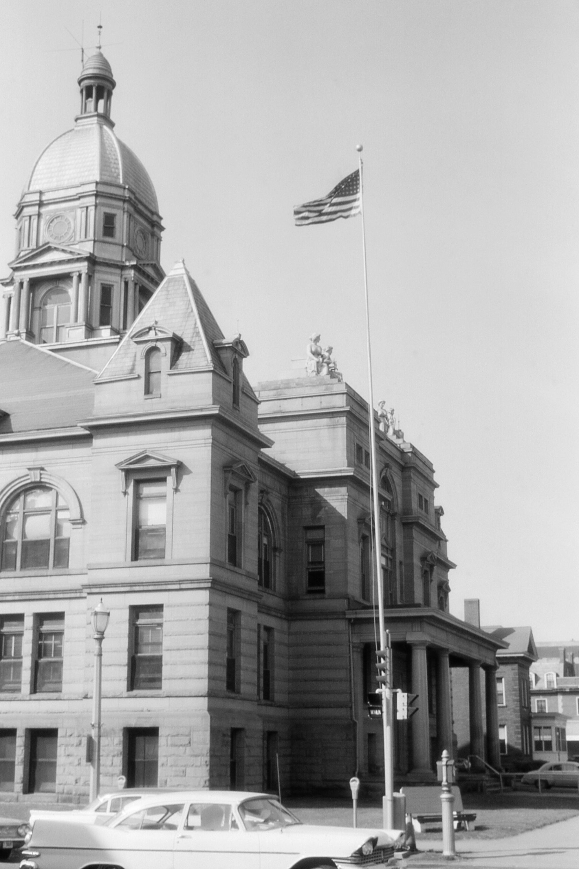 Historic courthouse gathering  with a dome, an American emblem  connected  a pole, and vintage cars parked successful  front