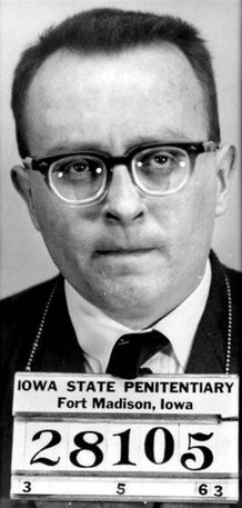 A black-and-white mugshot of a idiosyncratic   wearing glasses and a suit   with an Iowa State Penitentiary motion   below
