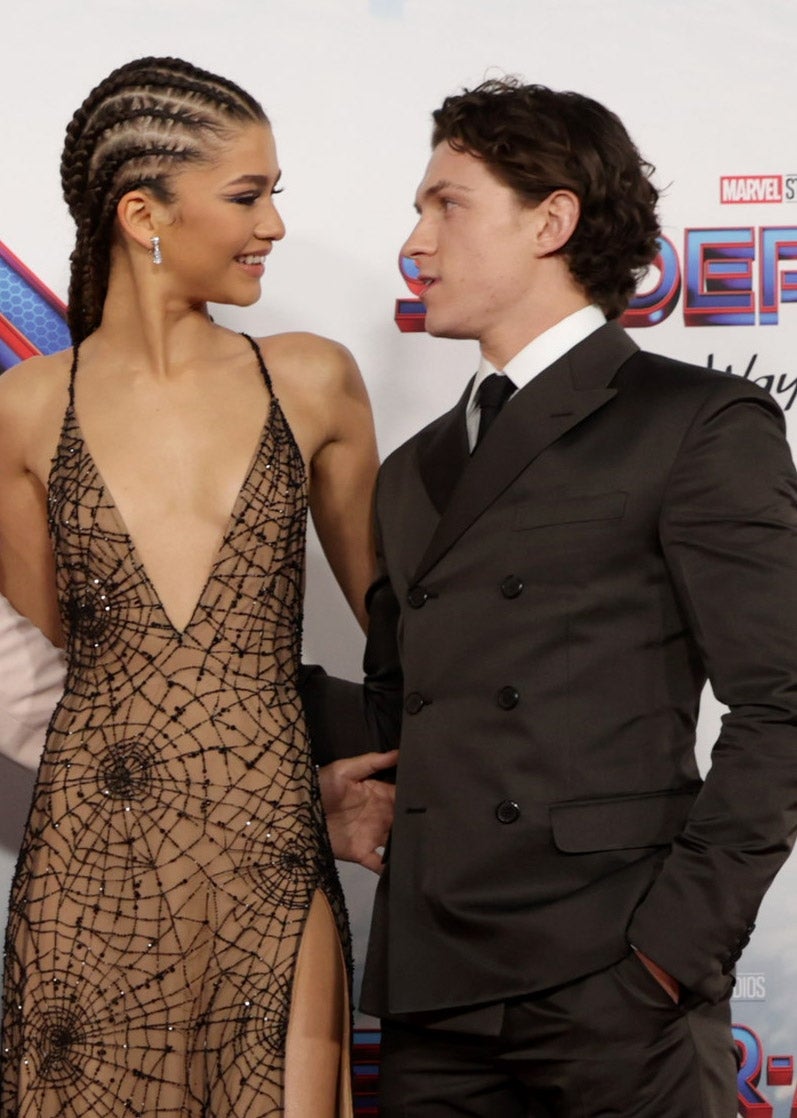 Two celebrities on a red carpet. One wears a web-patterned gown with a deep V-neck, the other wears a tailored suit