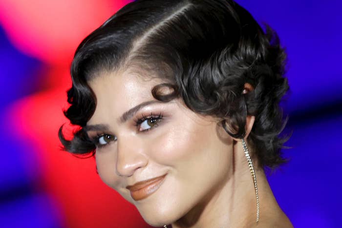 Celebrity in an elegant patterned gown with wavy hair at a formal event, vibrant abstract background