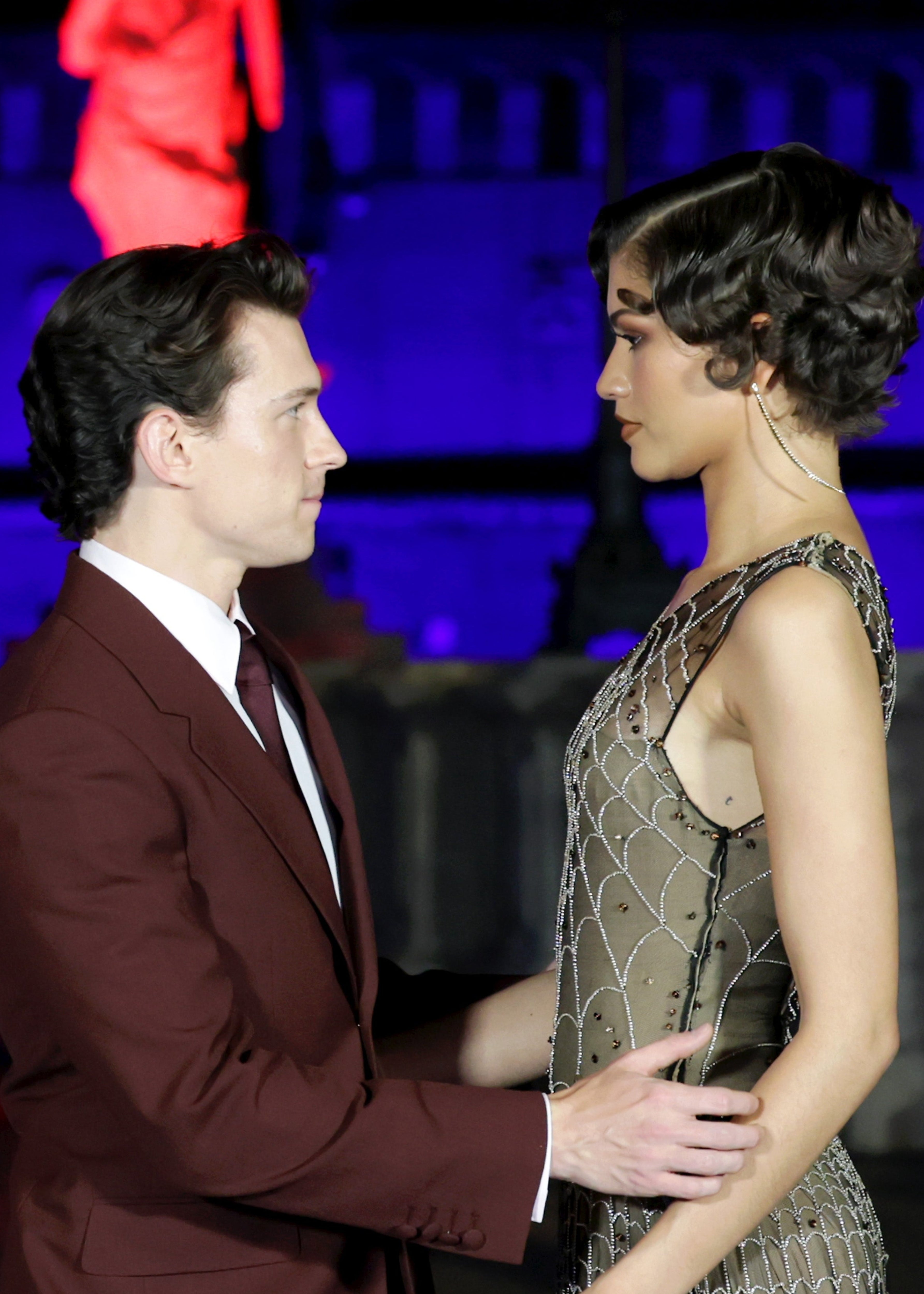 Two celebrities on a red carpet; one in a fitted suit and the other in an embellished gown, facing each other